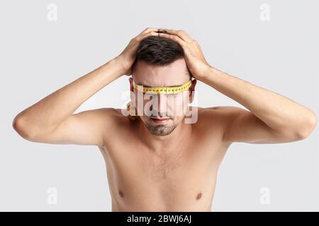 Uomo malato con nastro di misurazione su sfondo colorato. Concetto di anoressia Foto Stock