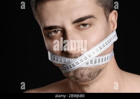 Uomo malato con nastro di misurazione su sfondo scuro. Concetto di anoressia Foto Stock