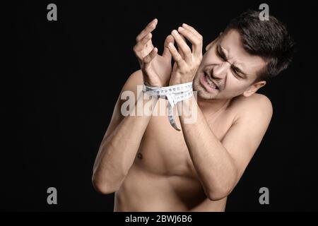 Uomo malato con nastro di misurazione su sfondo scuro. Concetto di anoressia Foto Stock