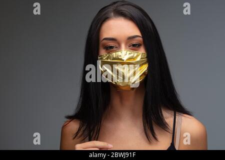 aumento di prezzo di maschere facciali e scarsità in COVID-19 volte concetto come una bella giovane donna che indossa una maschera facciale in oro perché può permetterselo Foto Stock