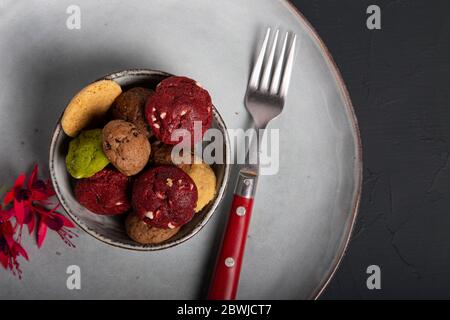 Primo piano di alcuni mini biscotti di vari sapori in una ciotola piccola su un piatto rustico verde. Immagine isolata. Foto Stock