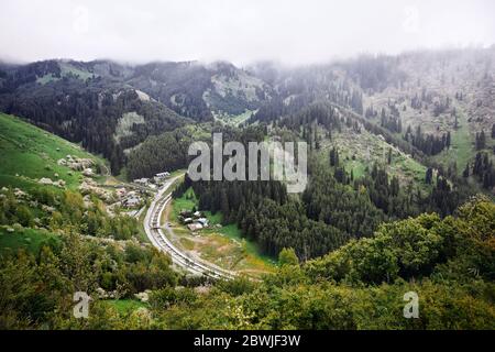 Vista aerea del villaggio alpino e del fiume in montagna a nubi nebbia. Foto scattata con il drone Foto Stock