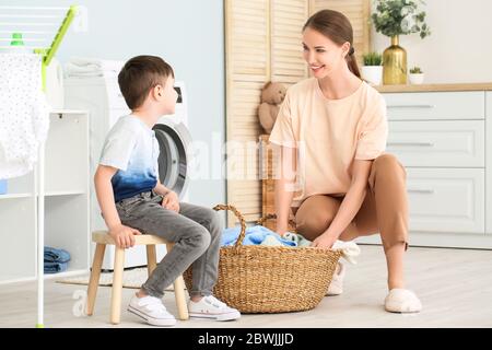 Giovane donna con il suo piccolo figlio che fa lavanderia a casa Foto Stock