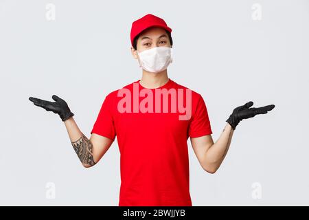 Migliori varianti. Amico sorridente asiatico di consegna ragazzo in uniforme rossa, cappuccio e t-shirt, sollevare le mani per tenere gli articoli, introdurre prodotti o pacchi corriere Foto Stock