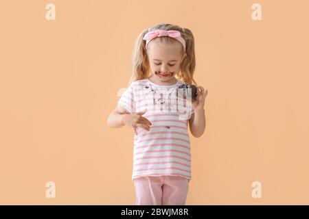 Bambina in vestiti sporchi mangiare torta di cioccolato su sfondo a colori Foto Stock