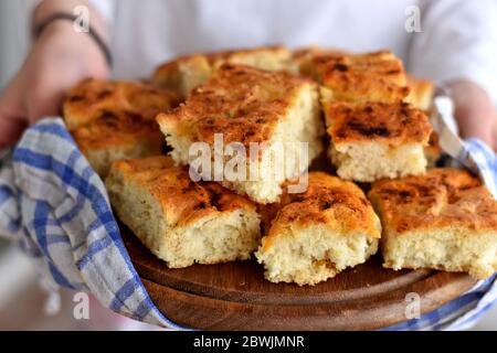 Mani femminili che tengono pane appena sfornato. Focaccia italiana fatta in casa con rosmarino e olio d'oliva. Appena sfornata e pronta a mangiare Foto Stock