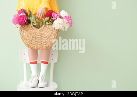 Giovane donna con bellissimi fiori di pony in borsa in piedi su sedia su sfondo colorato Foto Stock