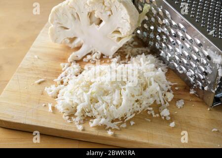 Grattugiare il cavolfiore con una grattugia metallica su un tavolo da cucina in legno, utilizzato come sostituto del riso per un sano pasto a basso contenuto di carb o dieta chetogena, selezionato fo Foto Stock