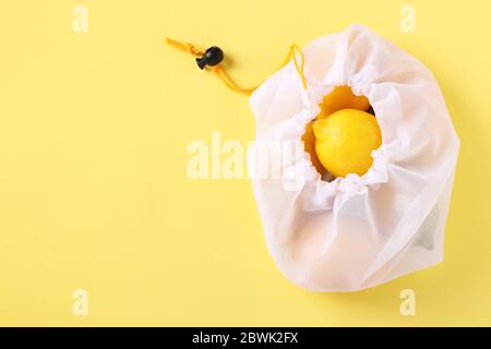 Limoni in sacchetto riutilizzabile eco-friendly mesh su sfondo giallo brillante. Concetto di zero rifiuti, arresto dell'inquinamento. Spazio di copia Foto Stock