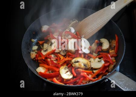 Tostatura di verdure come funghi e peperone rosso in una padella nera sulla stufa, sano concetto vegetariano, fuoco selezionato, profondità di campo stretta Foto Stock