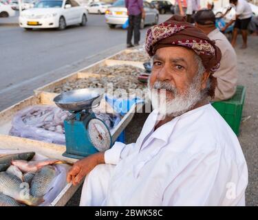 Anziano pescivendolo Omani che mostra un pesce al mercato del pesce stradale a Muscat, Sultanato dell'Oman. Foto Stock