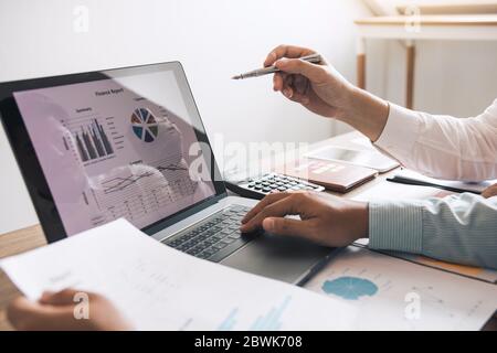 I colleghi parlano dei risultati dei documenti in mano e confrontano le informazioni finanziarie sullo schermo del notebook. Foto Stock
