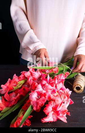 Le mani delle donne creare un mazzo di fiori di gladiolus per il giorno di San Valentino su un regalo Foto Stock