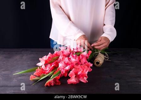 Le mani delle donne creare un mazzo di fiori di gladiolus per il giorno di San Valentino su un regalo Foto Stock