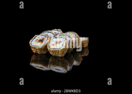 Un primo piano di panini fritti di sushi di cibo isolato su nero. Riflessione Foto Stock