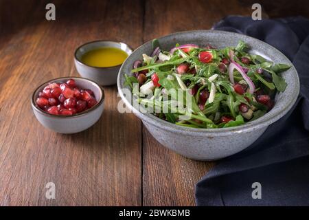 Arugula o insalata di razzo con semi di melograno e parmigiano in un recipiente su un tavolo di legno rustico scuro, fuoco selezionato, profondità di campo stretta Foto Stock