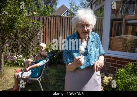 Donna anziana negli anni 80, con i suoi nipoti che si godono il sole nel suo giardino sul retro, Inghilterra, Regno Unito Foto Stock