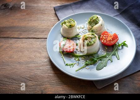 Panini di filetto di pesce di passera ripieni di purè di sedano e rucola, pomodori alla griglia, insalata di razzo e semi di sesamo su un piatto blu su un legno rustico Foto Stock