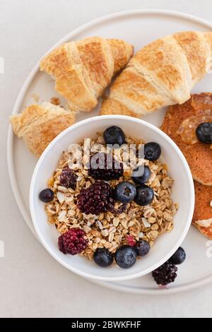 Immagine dall'alto di un piatto sano e nutriente per la colazione con muesli, frittelle d'avena e croissant. Composizione verticale. Foto Stock