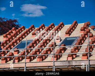 Un tetto di casa in costruzione, che mostra pile di piastrelle di terracotta pronte per essere calzate su listelli di legno. Una giornata di sole con un cielo blu. Foto Stock
