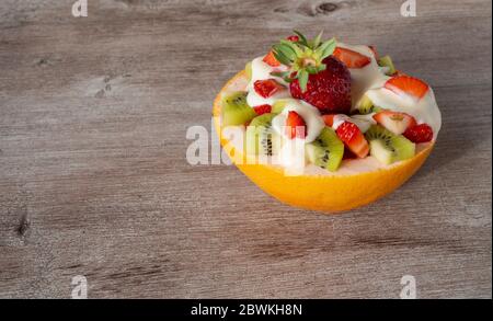 macedonia di frutta in una pentola di pompelmo. frutta su fondo di legno. Foto Stock