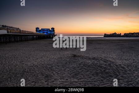 Il tramonto getta un bagliore rosso dietro il Grand Pier e la spiaggia ricostruiti di Weston-Super-Mare. Foto Stock