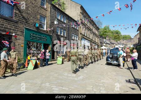 I re-attori vestiti come soldati della Guardia domestica che marciano in una colonna su Main Street, Haworth, West Yorkshire durante il fine settimana del villaggio 1940 s. Foto Stock