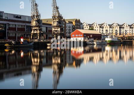 Bristol, Inghilterra, Regno Unito - 25 maggio 2020: La luce del mattino splende sulle gru portuali, i magazzini, le barche storiche e i moderni edifici di appartamenti sul posto di Bristol Foto Stock