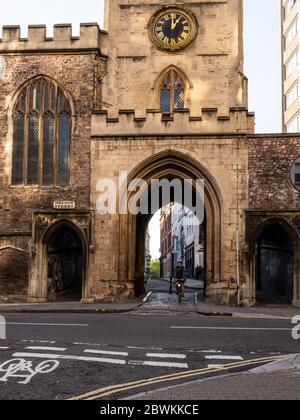 Bristol, Inghilterra, Regno Unito - 25 maggio 2020: Un ciclista attraversa la porta d'ingresso dell'arco gotico della chiesa di San Giovanni sul Muro, parte delle mura medievali di BRI Foto Stock