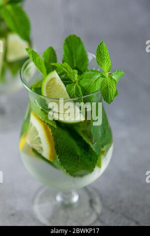 Mojito estivo con menta e calce rinfrescante cocktail con rum e ghiaccio in vetro su sfondo grigio. Cocktail mojito su tavolo in pietra. Vetro glassy alto per bevande Foto Stock