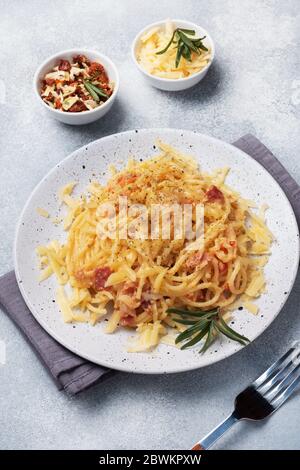 Spaghetti di pasta con formaggio a base di uova di pancetta su un piatto con spezie. Piatto tradizionale italiano Carbonara. Tavolo in cemento grigio. Foto Stock