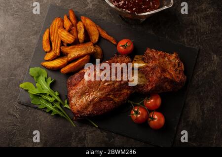 Costolette fritte con rucola, patate rustiche, cipolla, salsa di pomodori su tavola rotonda. Sfondo scuro. Foto Stock
