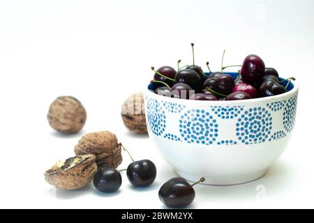 Ciotola blu e bianca con ciliegie fresche decorate con noci secche su sfondo bianco Foto Stock