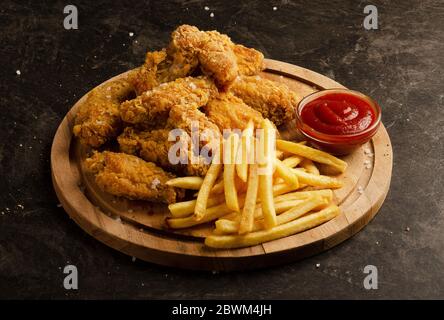 Ali di pollo fritte, patatine fritte e salsa di ketchup su sfondo scuro Foto Stock