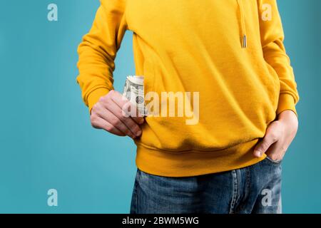 il ragazzo giovane toglie o mette i soldi in una tasca di una felpa gialla Foto Stock