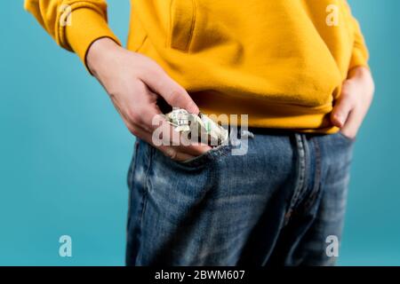 il ragazzo giovane toglie fuori o mette i dollari crumpled nel suo tasca in jeans Foto Stock
