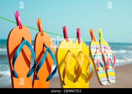 chiusura di alcune diverse coppie di colorati infradito appesi su una linea di vestiti sulla spiaggia, con il mare sullo sfondo Foto Stock