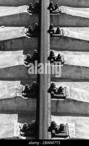 Rusty rail su traversine di calcestruzzo. Sfondo verticale bianco e nero Foto Stock