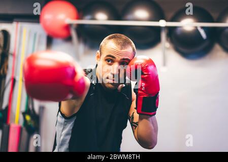 Pugile latino con guanti rossi che lo gettano direttamente da destra in palestra. Combatti concetto Foto Stock