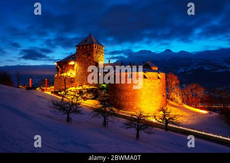 Vaduz, Liechtenstein. Castello illuminato di Vaduz, Liechtenstein al tramonto - famoso punto di riferimento durante la notte, con il cielo al tramonto, montagne in background Foto Stock