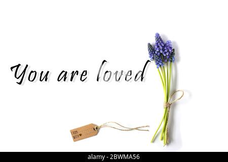 Fiori blu primavera con tag regalo e segno che siete amati. Concetto romantico, gentile, ispirato messaggio d'amore Foto Stock