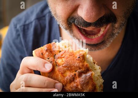 L'uomo Mustachioed tiene il pane ed è pronto a morso il pane. L'uomo apre la bocca per mangiare pane. Foto Stock