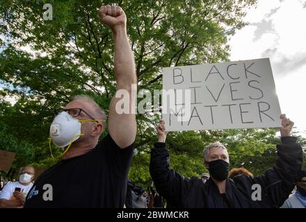 Un uomo tiene un pugno sollevato come segno di solidità con la comunità afroamericana, come una donna tiene un segno di sostegno durante una veglia e venire toge Foto Stock