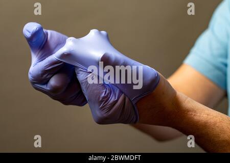 Passaggio di mano a buttare via il blu guanti monouso medicali, isolati su sfondo bianco. Controllo delle infezioni del concetto. Foto Stock