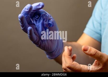 Passaggio di mano a buttare via il blu guanti monouso medicali, isolati su sfondo bianco. Controllo delle infezioni del concetto. Foto Stock