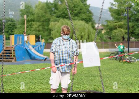 Ragazzo che indossa occhiali di protezione chirurgici vestiti in una camicia di plaid davanti ad un nastro di barriera a strisce rosse e bianche intorno al parco giochi. Foto Stock