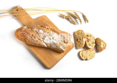 Baguette a metà fette o pane francese cotto con cipolle su un tavolo da cucina e alcune orecchie di grano isolate con ombre su uno sfondo bianco, spazio copia, Foto Stock