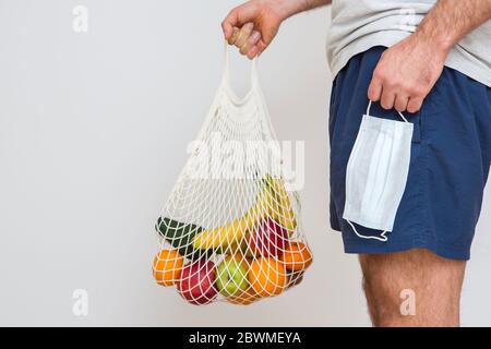 Concetto di zero sprechi con spazio di copia. Mano da uomo che tiene una borsa della spesa in rete con prodotti. Acquirente eco-compatibile in mesh. Sfondo bianco, primo piano. Plas Foto Stock