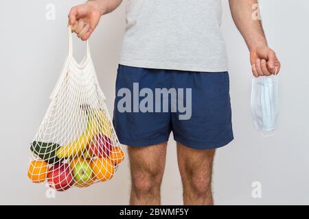 Concetto di zero sprechi con spazio di copia. Mano da uomo che tiene una borsa della spesa in rete con prodotti. Acquirente eco-compatibile in mesh. Sfondo bianco, primo piano. Plas Foto Stock