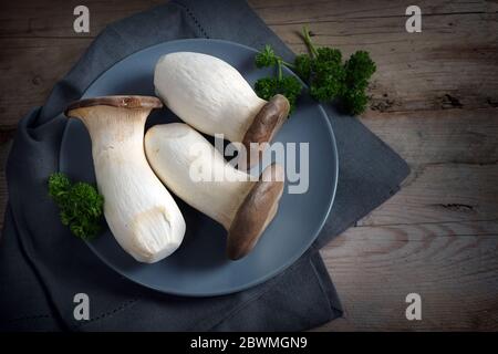 Funghi di ostriche del re, il Pleurotus eryngii, su un piatto blu e un tavolo rustico di legno scuro, spazio di copia, vista ad angolo alto dall'alto Foto Stock